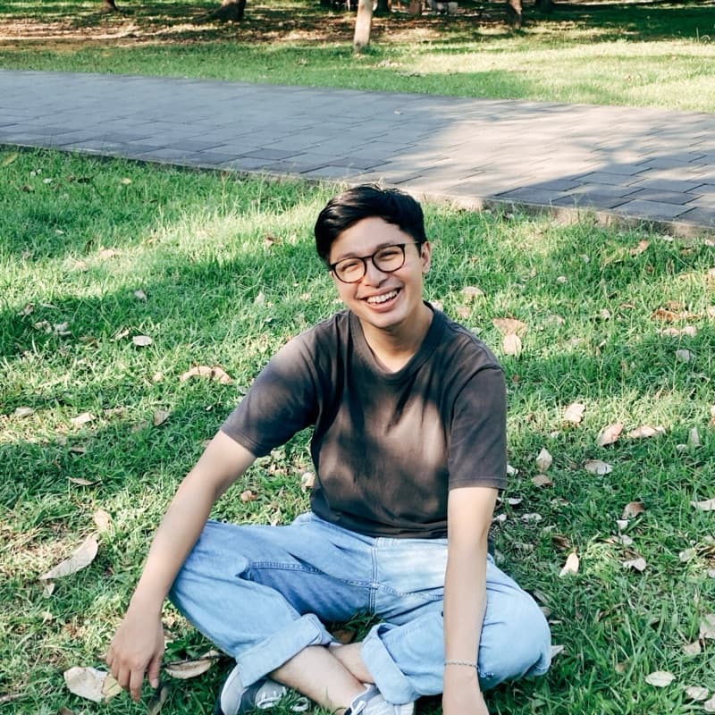 Alex sitting cross-legged on the grass, smiling at the camera